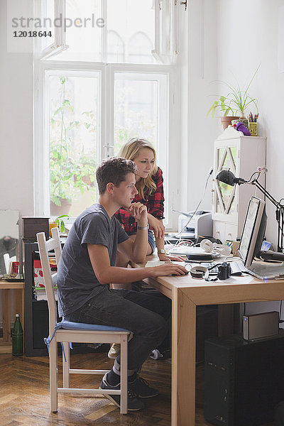 Junges Paar mit Computer am Tisch gegen Fenster
