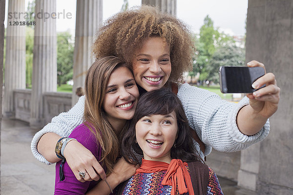 Lächelnde junge Frau nimmt Selfie mit weiblichen Freunden mit.