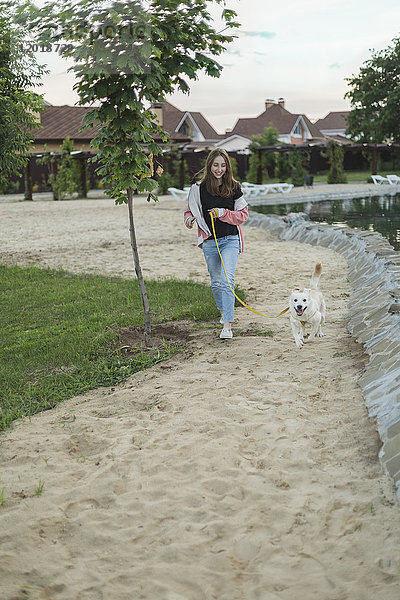 Lächelndes Teenagermädchen läuft mit Hund auf Sand