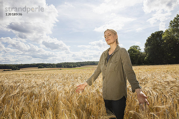 Nachdenkliche Frau steht inmitten von Weizenfeldern auf dem Bauernhof gegen den Himmel an einem sonnigen Tag.