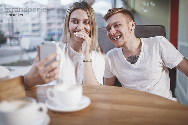 Glückliches junges Paar,  das im Restaurant auf sein Handy schaut.