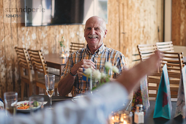 Lächelnder älterer Mann,  der einen Freund ansieht,  während er am Tisch im Restaurant sitzt.