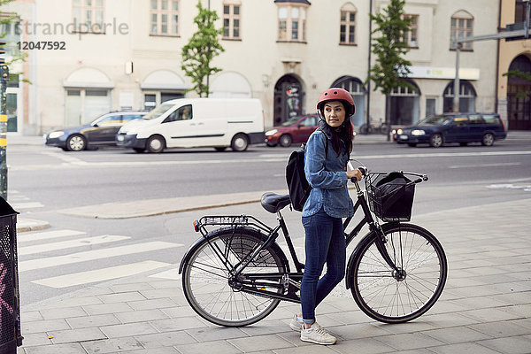 Mittlere erwachsene Frau stehend mit Fahrrad auf dem Bürgersteig in der Stadt
