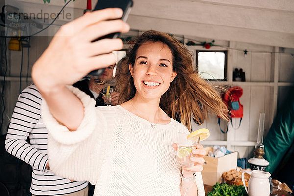 Junge Frau nimmt Selfie auf Smartphone mit Freunden in der Hütte