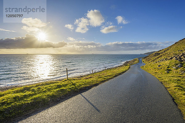 Typische schottische Landschaft auf der Isle of Skye mit einer Küstenstraße und der Sonne,  die über dem Meer scheint,  Schottland,  Vereinigtes Königreich