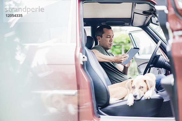 Mann mit Tablette im Auto mit Hund auf Beifahrersitz