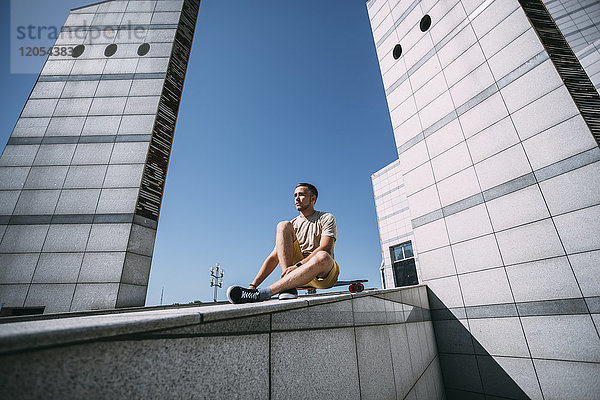 Junger Mann mit Longboard umgeben von moderner Architektur