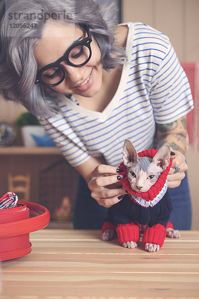 Frau,  die zu Hause einen Pullover auf ihre Sphynx-Katze zieht.