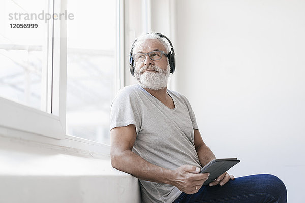 Erwachsener Mann mit Tablette und Kopfhörer aus dem Fenster schauend