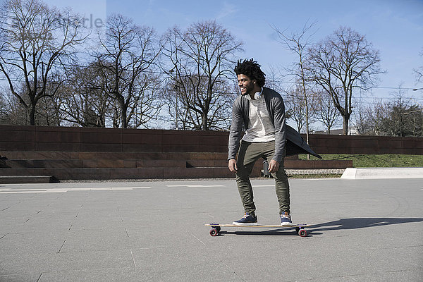Lächelnder junger Mann auf dem Longboard im Skatepark