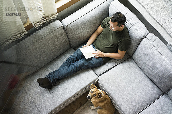 Mann zu Hause mit Tablette auf der Couch mit Hund neben ihm