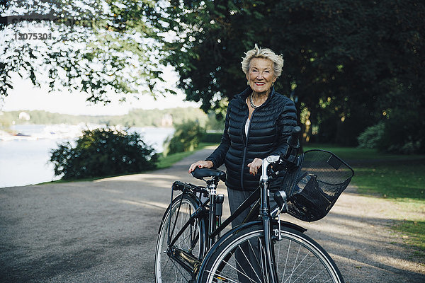 Porträt einer lächelnden Seniorin mit Fahrrad im Park