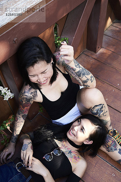 Tätowiertes lesbisches Paar lacht und hat Spaß auf einer Holzbrücke.