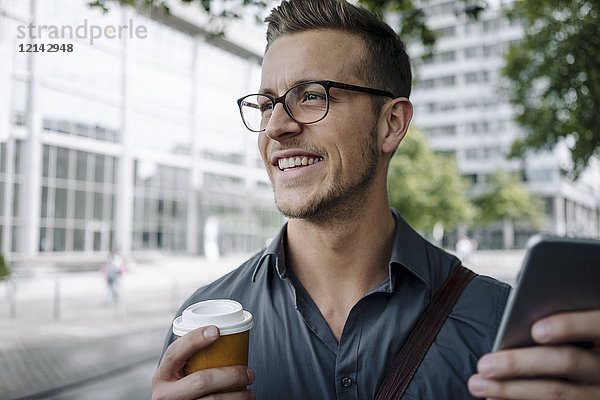 Porträt eines lachenden jungen Geschäftsmannes mit Kaffee zum Mitnehmen und Smartphone