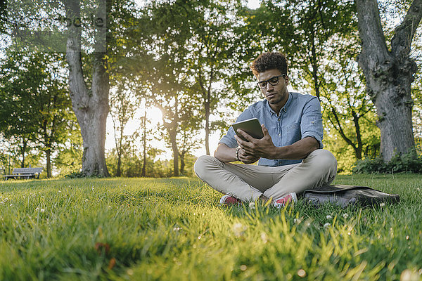 Junger Mann sitzend im Park mit mobilem Gerät