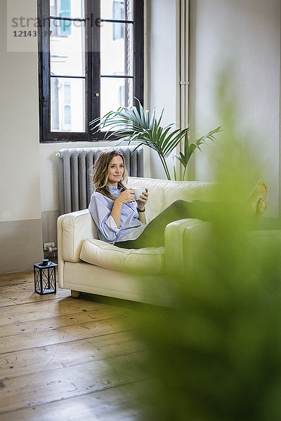 Frau entspannt sich auf der Couch zu Hause beim Kaffeetrinken