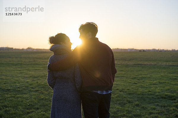 Junges Paar,  das bei Sonnenuntergang auf einer Wiese spazieren geht.