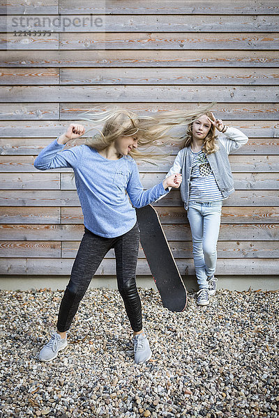 Zwei Mädchen mit Skateboard vor Holzfassade
