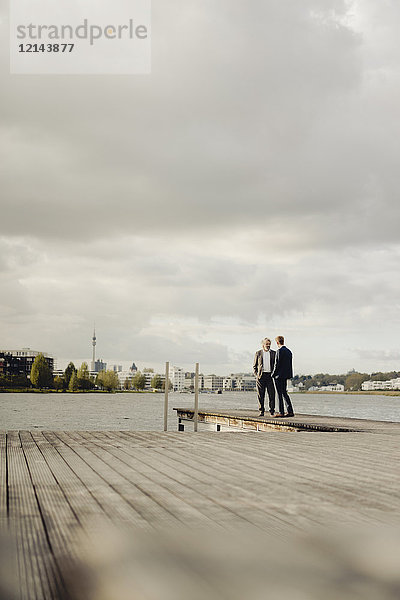 Zwei Geschäftsleute,  die auf einem Steg am See stehen und reden.