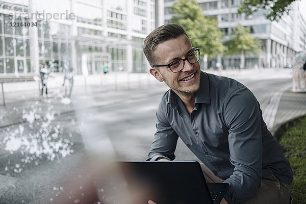Porträt eines lachenden jungen Geschäftsmannes mit Laptop im Freien