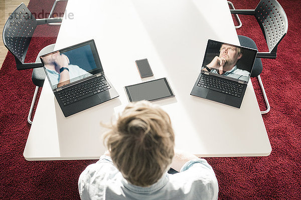 Geschäftsmann mit zwei Laptops,  die Bilder von sich selbst zeigen.