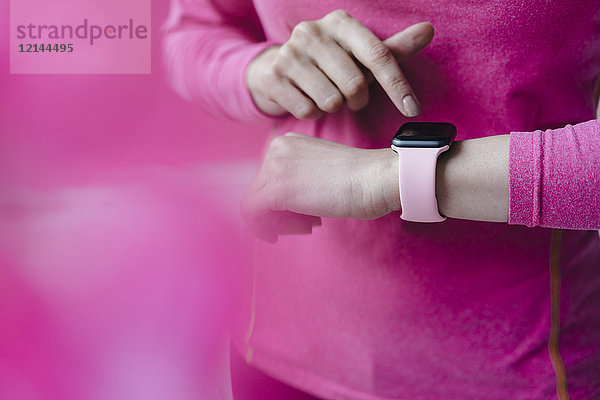 Nahaufnahme einer Frau in rosa Sportbekleidung,  die ihre Smartwatch anpasst.
