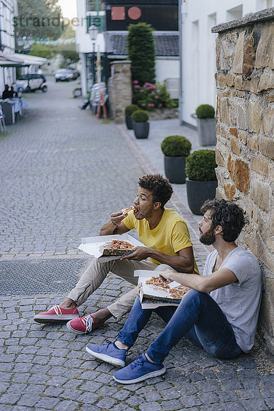 Zwei Freunde essen Pizza zum Mitnehmen in der Stadt