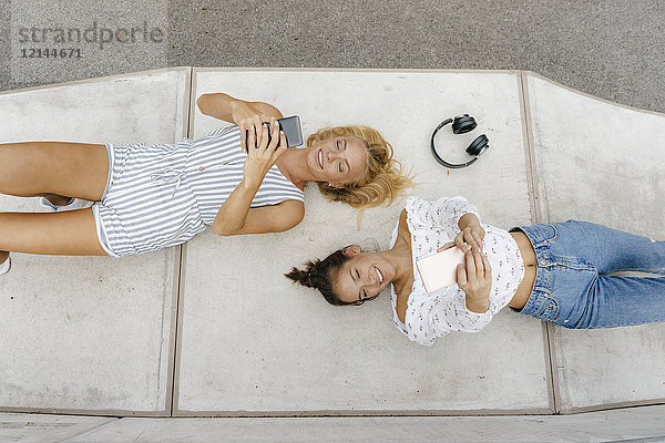 Zwei glückliche junge Frauen mit Handys auf einer Rampe in einem Skatepark.