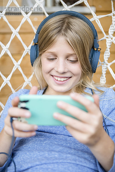 Portrait des glücklichen Mädchens mit Kopfhörer und Smartphone im Hängesessel