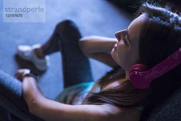 Fröhliche junge Frau mit rosa Kopfhörern,  die nachts in der modernen Stadt Musik hört.
