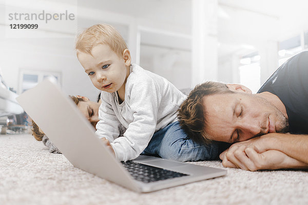 Eltern schlafen mit einem kleinen Mädchen und benutzen einen Laptop auf dem Boden.
