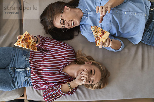 Zwei lachende junge Frauen,  die zusammen Pizza essen.