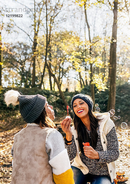 Zwei hübsche Frauen haben Spaß mit Seifenblasen im herbstlichen Wald