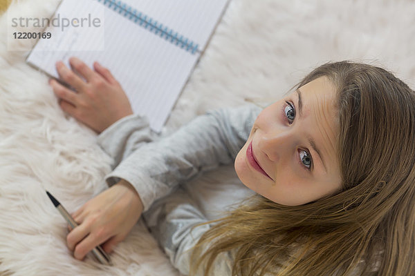 Porträt eines lächelnden Mädchens,  das mit Bleistift und Broschüre auf dem Boden liegt.