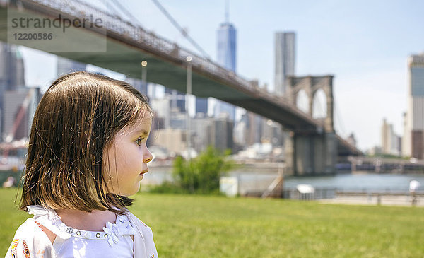 USA,  New York,  Brooklyn,  Porträt des kleinen Mädchens im Park mit Blick auf die Brooklyn Bridge im Hintergrund