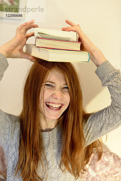 Porträt eines lachenden rothaarigen Mädchens mit einem Stapel Bücher auf dem Kopf.