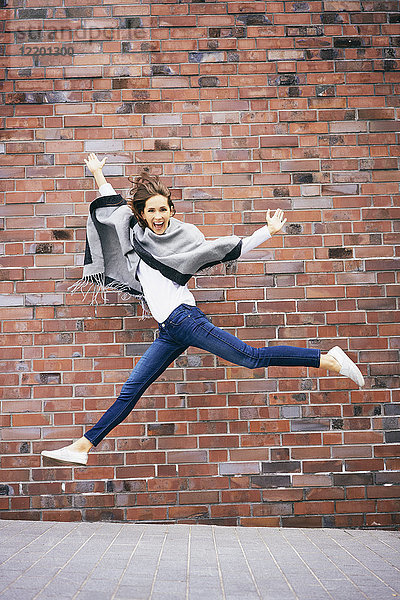 Fröhliche junge Frau,  die vor der Ziegelmauer in die Luft springt.