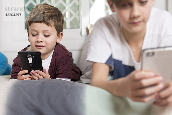 Zwei Jungen,  die zu Hause auf dem Bett liegen und Handys benutzen.
