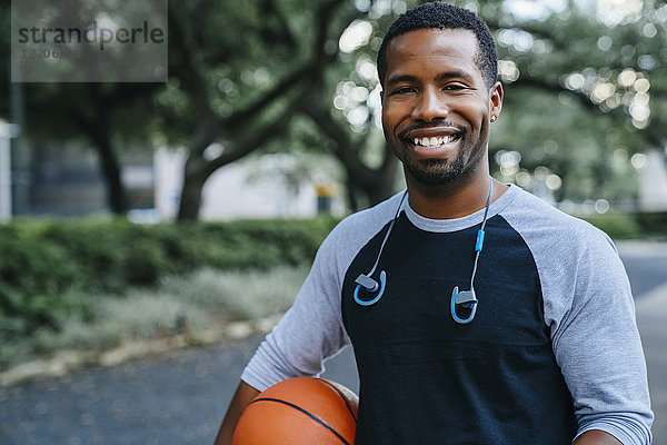 Porträt eines lächelnden schwarzen Mannes,  der einen Basketball hält