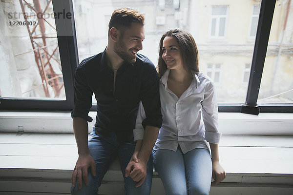 Kaukasisches Paar sitzt auf der Fensterbank und hält sich an den Händen
