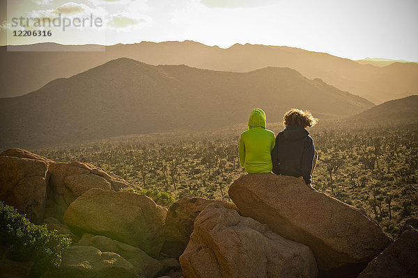 Jungen sitzen auf einem Felsen und bewundern die Wüstenlandschaft