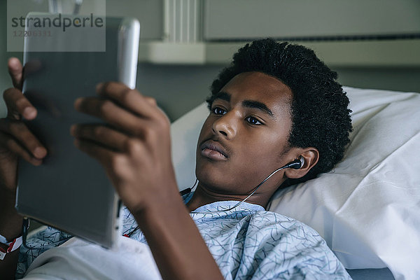Schwarzer Junge liegt im Krankenhausbett und hört einem digitalen Tablet zu