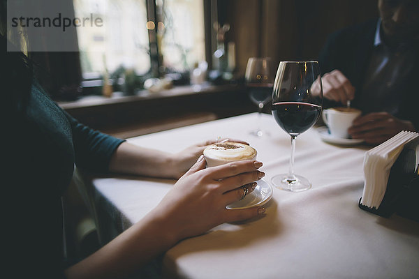 Hände eines kaukasischen Paares beim Trinken von Kaffee und Wein