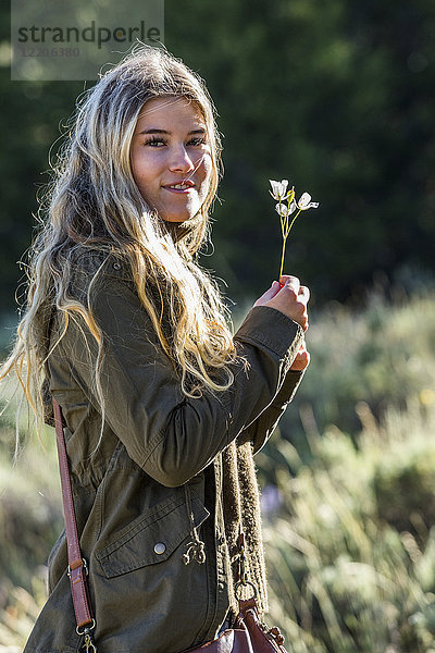 Porträt eines lächelnden kaukasischen Mädchens,  das eine Wildblume hält