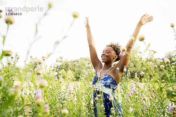 Lächelnde gemischtrassige Frau,  die in einem Feld mit Wildblumen feiert