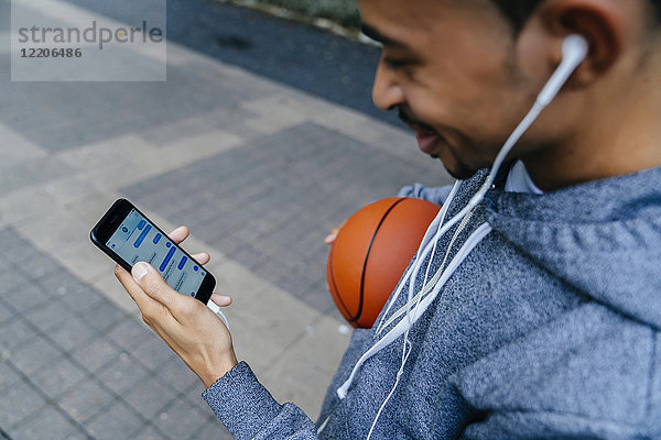 Schwarzer Mann hält Basketball und hört Handy mit Ohrhörern