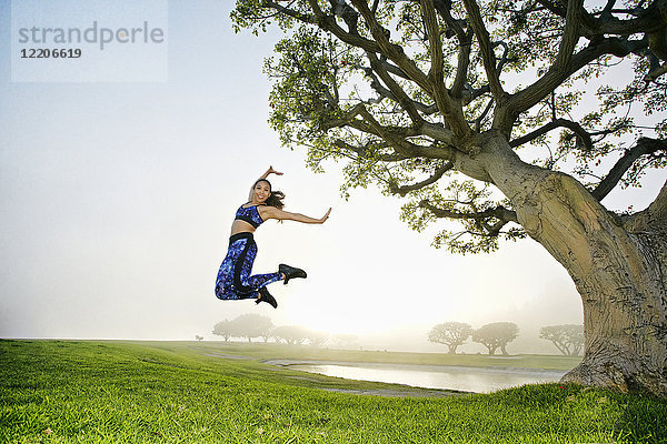 Gemischtrassige Frauen springen auf einem Feld in der Nähe eines Baumes