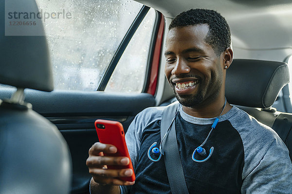 Lächelnder schwarzer Mann,  der im Auto eine SMS auf seinem Handy schreibt