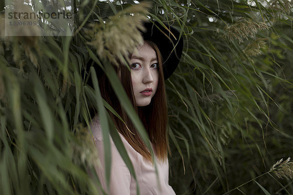 Porträt einer ernsten asiatischen Frau,  die in einem Feld mit hohem Gras steht