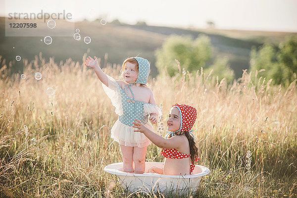 Zwei Mädchen auf dem Feld,  die in einer Plastikwanne mit Wasser spielen